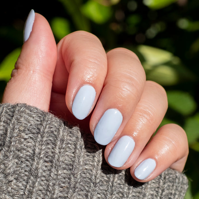 Hand with nails neatly painted in BP, a pastel icy light blue gel polish for a smooth at-home manicure