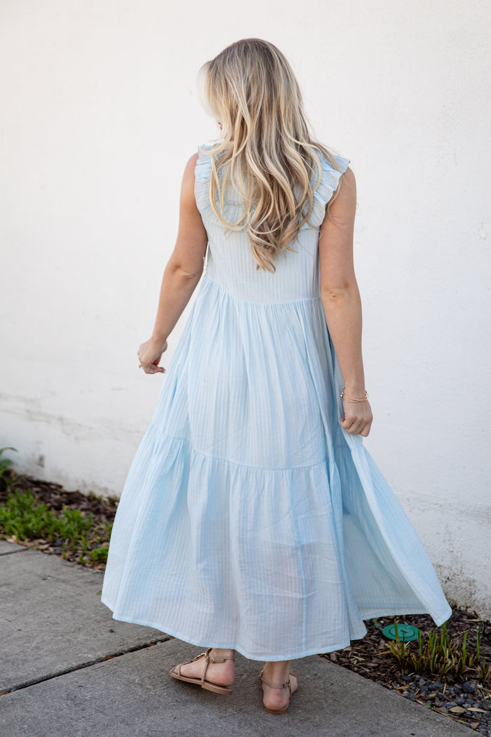 Woman wearing a light blue dress against a white wall.