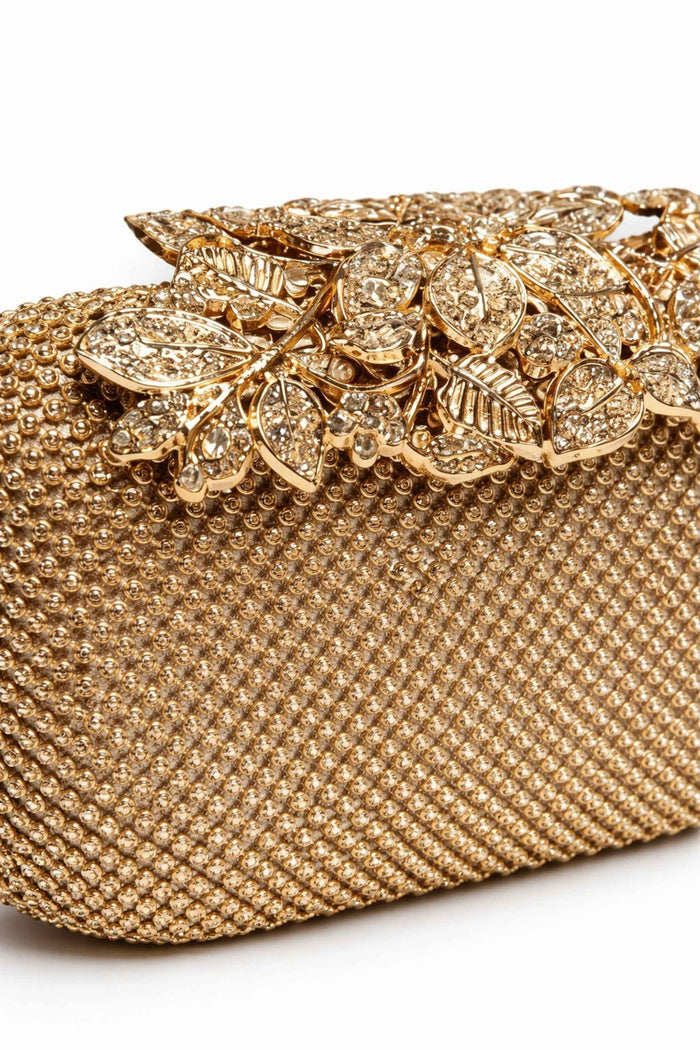 Close-up of the gold-tone beaded surface and floral embellishment on the gold flower clip clutch, showcasing sparkling rhinestones and detailed craftsmanship.
