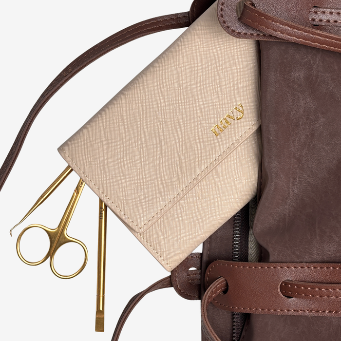 Close-up of a brown leather bag with a beige pouch and gold scissors on a light gray background
