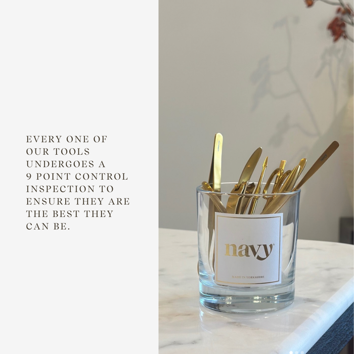 Glass container with gold utensils labeled 'navy' on a marble surface.