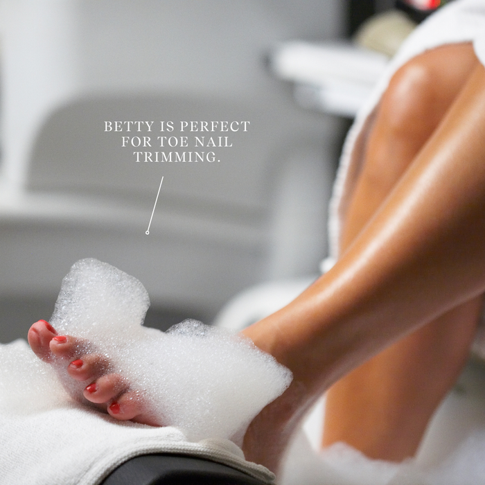Person with feet in a bubble bath, wearing a towel, with text 'Betty is perfect for toe nail trimming'.
