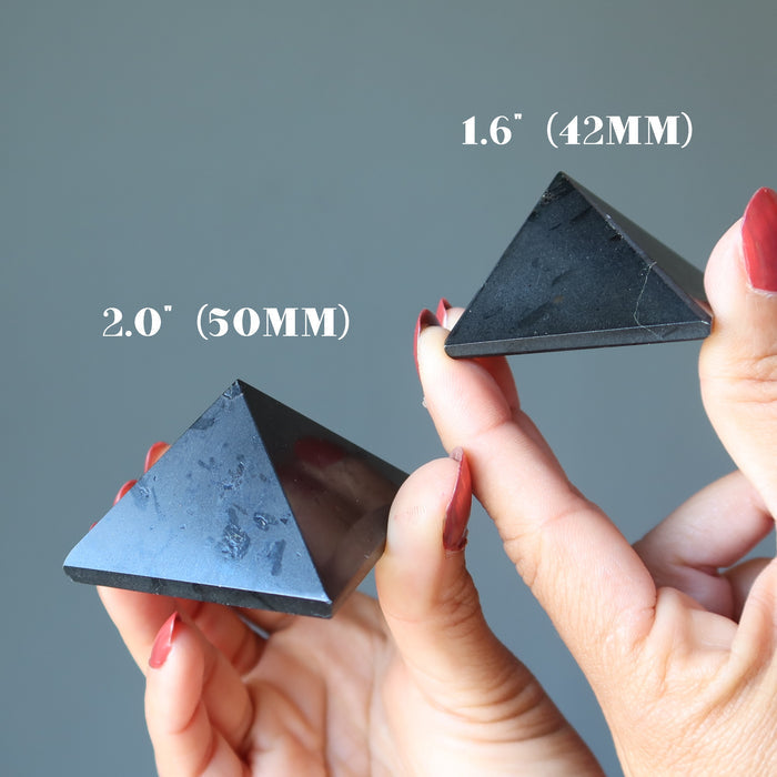 hands holding two black tourmaline pyramids to show size difference