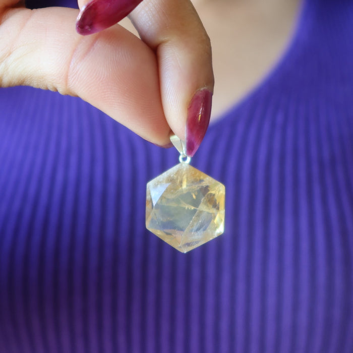 Hand holding a faceted Citrine crystal pendant against a purple background