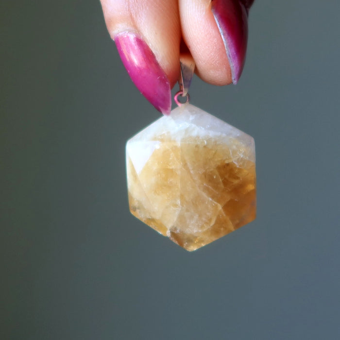 Citrine pendant held by a hand with pink nail polish against a gray background