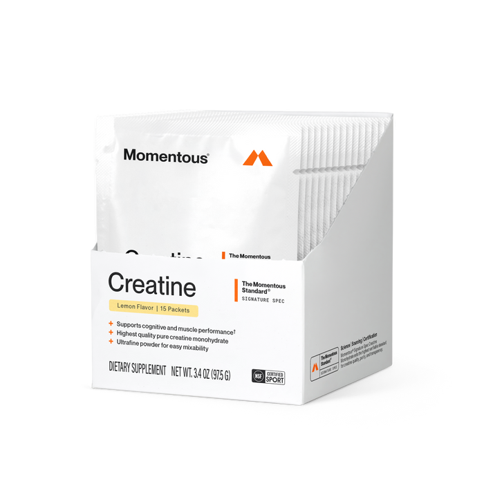 A white box containing 15 individual Momentous Creatine Monohydrate single-serve powder packets in Lemon Flavor. The front of the box displays the Momentous logo and orange mountain icon, a yellow "Lemon Flavor | 15 Packets" badge, and an orange "The Momentous Standard Signature Spec" label. Three bullet points list product benefits: supports cognitive and muscle performance, highest quality pure creatine monohydrate, and ultrafine powder for easy mixability. Net weight is 3.4 oz (97.5g).