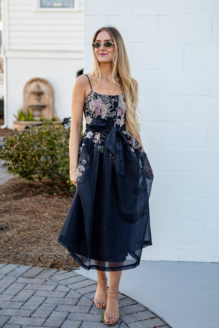 Woman wearing a floral dress standing against a white wall.