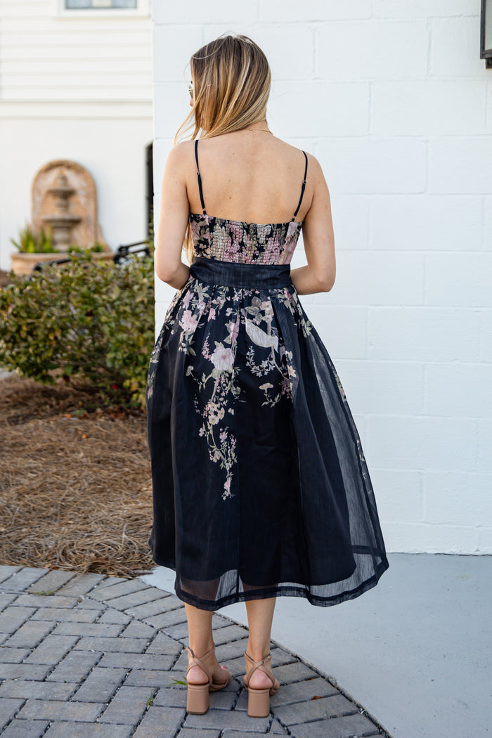Woman wearing a floral dress with a white wall and garden in the background