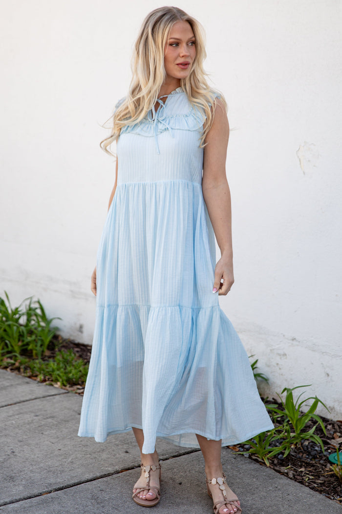 Woman wearing a light blue dress standing against a white wall.
