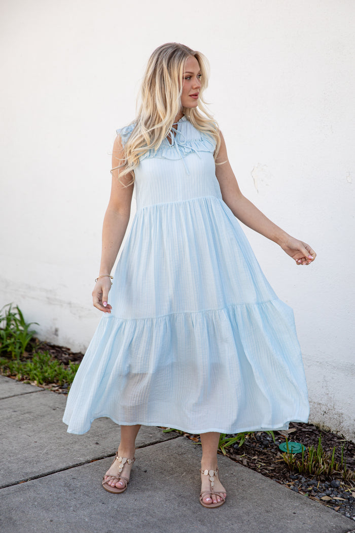 Woman wearing a light blue dress standing against a white wall.