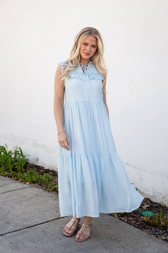 Woman wearing a light blue dress standing against a white wall.