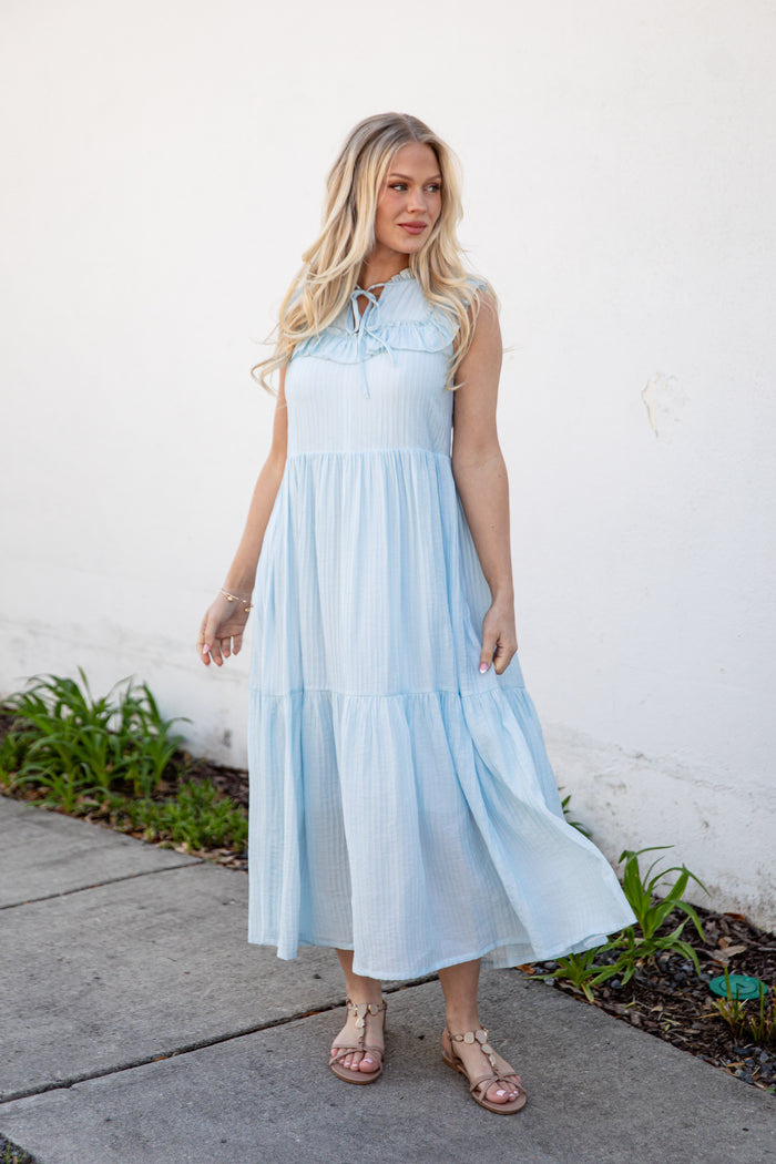 Woman wearing a light blue dress standing against a white wall.
