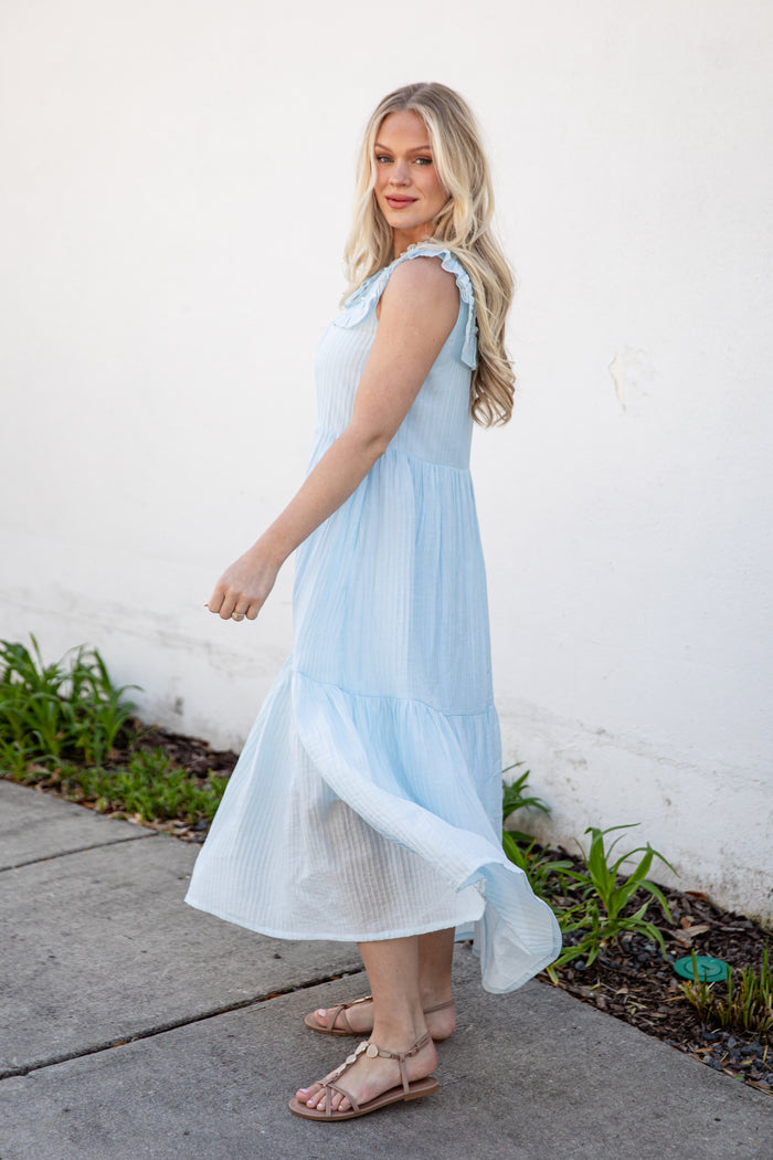 Woman wearing a light blue dress standing on a sidewalk with a white wall in the background