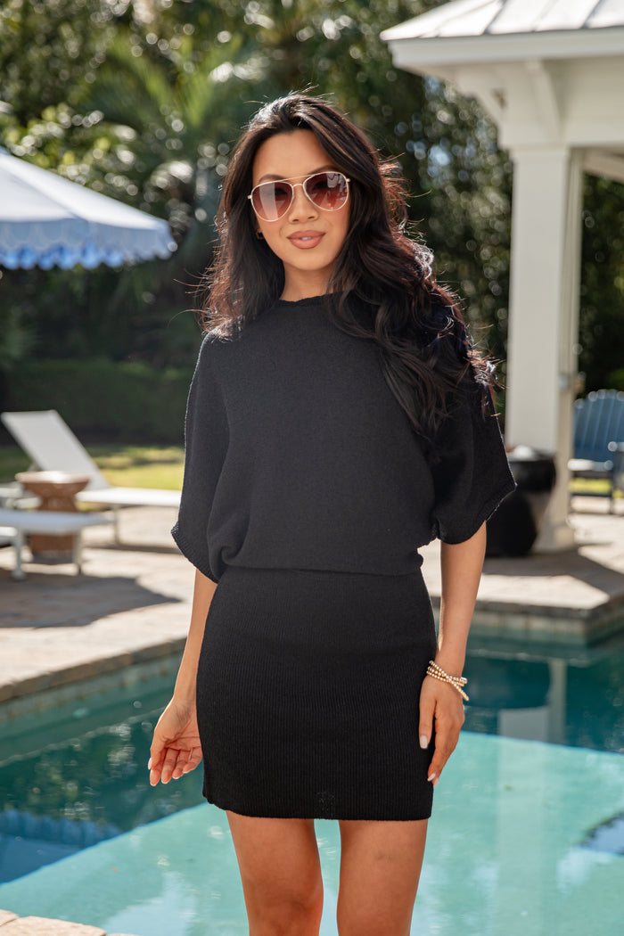 Woman in a black outfit standing by a pool with sunglasses on