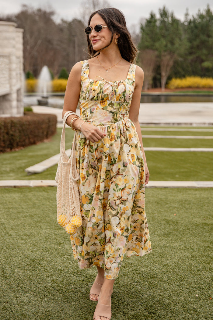 Woman in a floral dress standing on grass with a fountain in the background