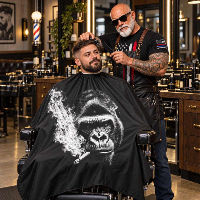 buybarber.com charachter in a barber chair gets a haircut from a tattooed barber wearing sunglasses and an apron. The barber is wearing a black apron over a black t-shirt with a red, white, and blue American flag graphic.