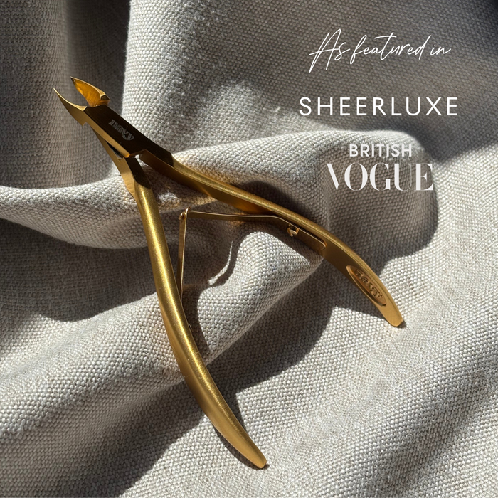 Gold nail clippers on a textured gray background with 'Sheerluxe' and 'British Vogue' text.