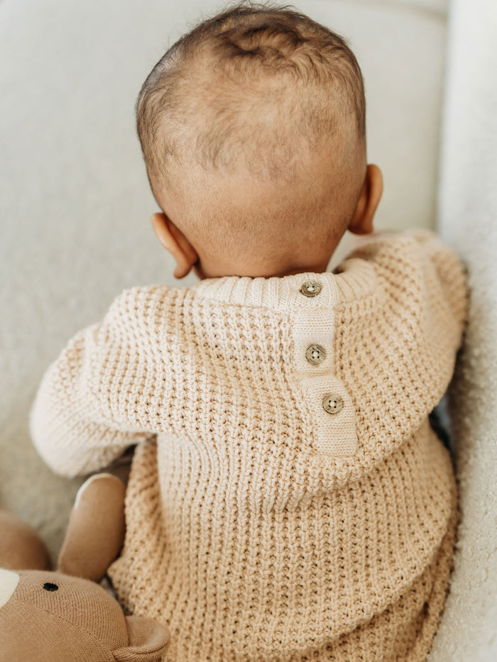 Baby wearing beige Viverano Organics baby top made from organic cotton with button details on back