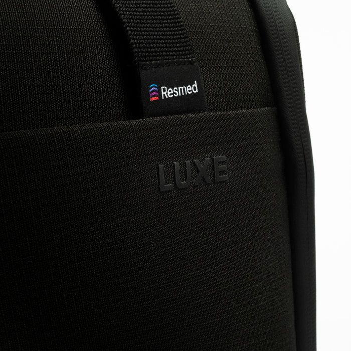 Close-up of a black CPAP insert with a visible Resmed logo patch on the strap and embossed LUXE branding on the front pocket.