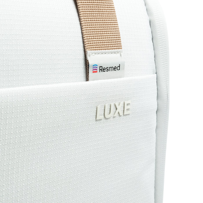 Close-up of the CPAP insert bag with a beige webbing strap and a small white Resmed label, plus an embossed LUXE logo on the front pocket.