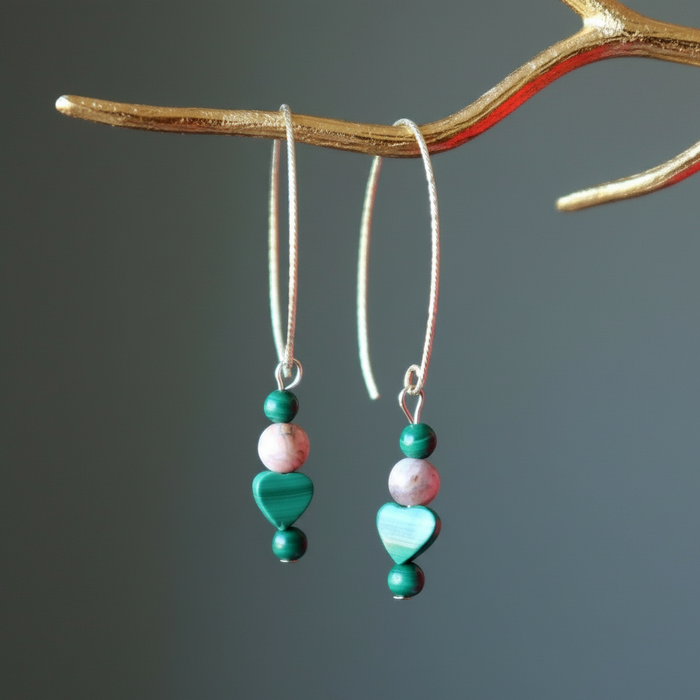 Pair of earrings with green and pink beads hanging from a branch against a gray background