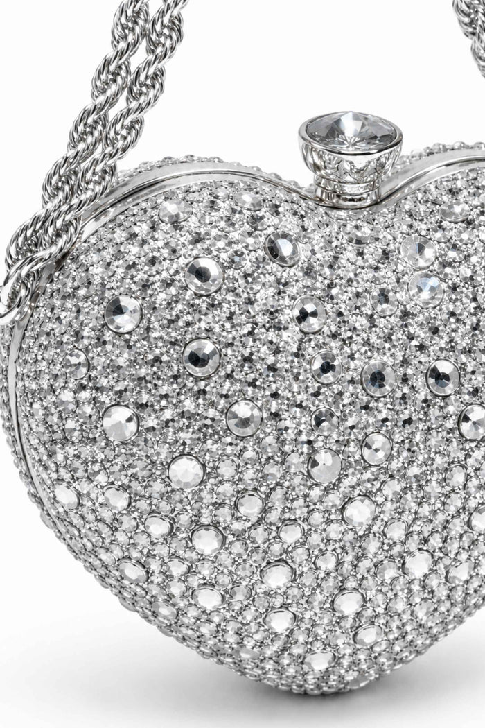Close-up of rhinestone-encrusted silver clutch with a large clear gemstone clasp and twisted silver chain handle, luxurious evening bag