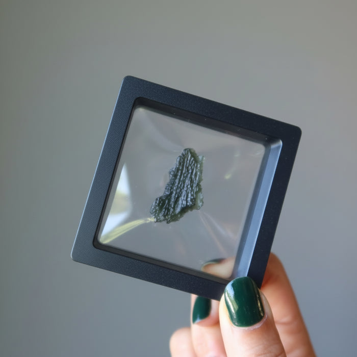 hand holding raw moldavite in suspension display case