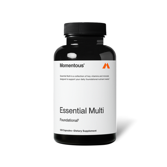 Black bottle of Momentous Essential Multi capsules centered on a transparent background. Text on the label reads: “Momentous®” “Essential Multi is a collection of key vitamins and minerals designed to support your daily foundational nutrient needs.*” “Essential Multi” “Foundational†” “120 Capsules—Dietary Supplement”
