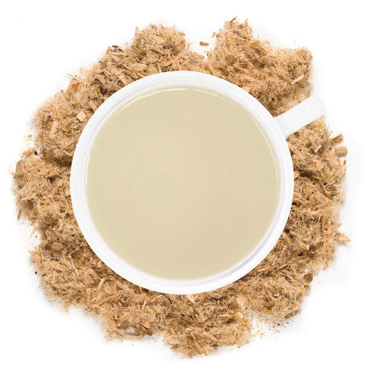 White mug filled with Slippery Elm Tea with slippery elm herb around the cup.