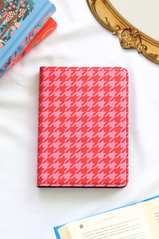 Pink houndstooth patterned kindle on a white surface with books and a decorative object in the background.