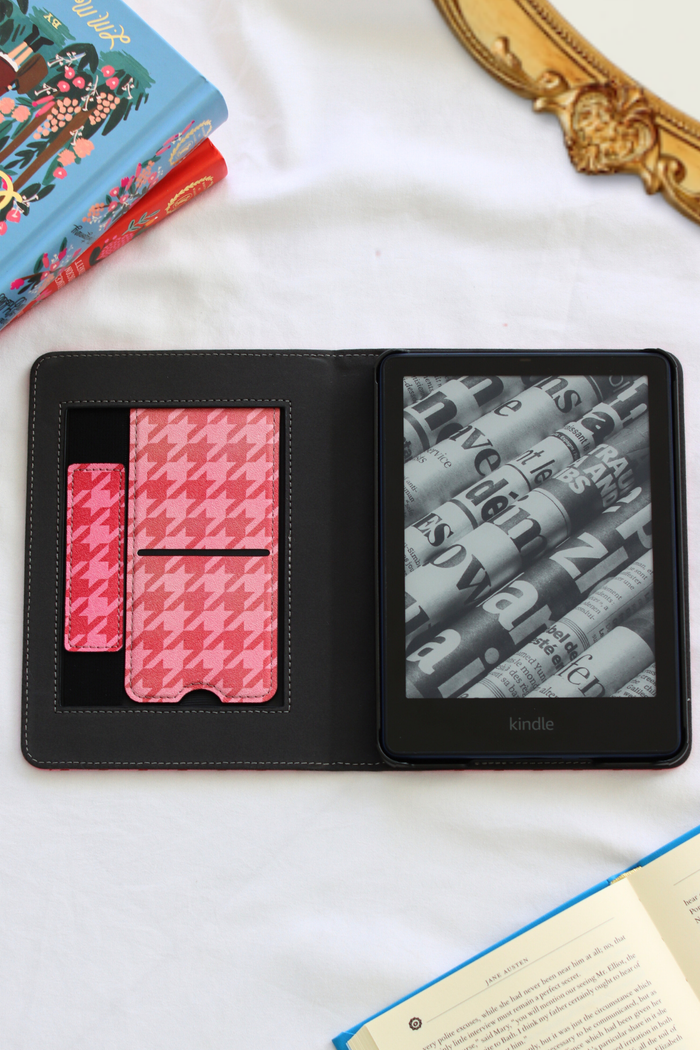 Kindle device with pink houndstooth case on a white surface with books in the background