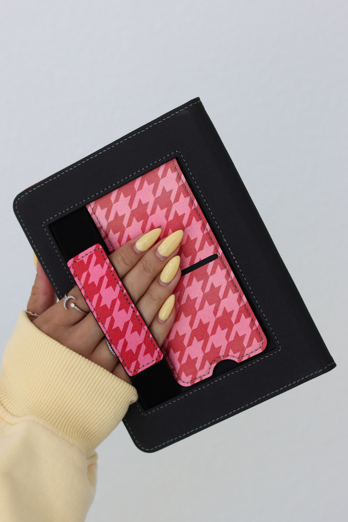 red kindle with pink houndstooth patterned held by a hand against a light gray background