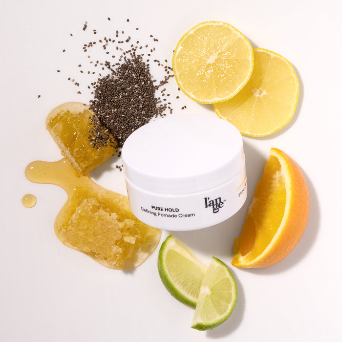 L’ange Pure Hold Defining Pomade Cream jar surrounded by citrus slices, honey, and chia seeds