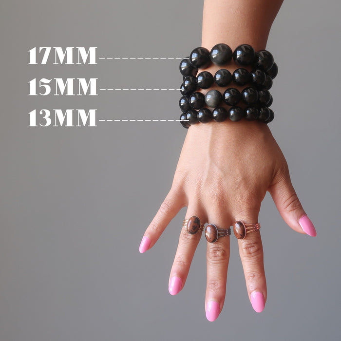 hand wearing mahogany obsidian rings and a stack of rainbow obsidian beaded stretch bracelets showing different bead sizes