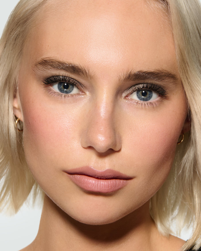 Close-up of a model's face against a neutral background, wearing Selene Liquid Lurex Liquid Eyeshadow, a tarnished, cool toned greenish/silver.