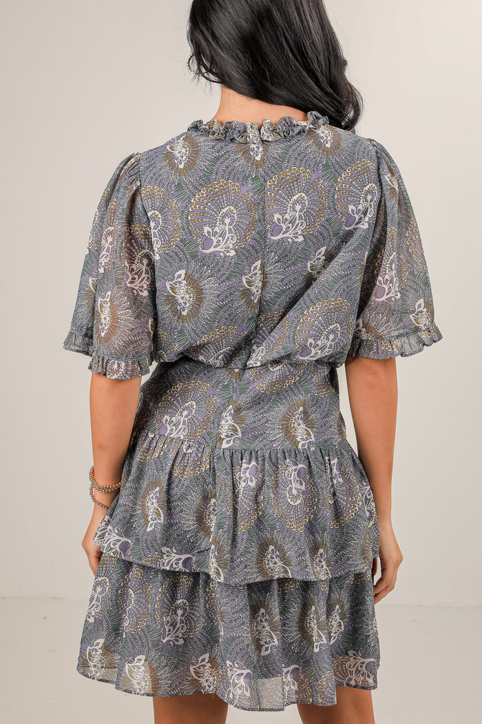 Woman wearing a patterned dress with ruffled layers on a plain background