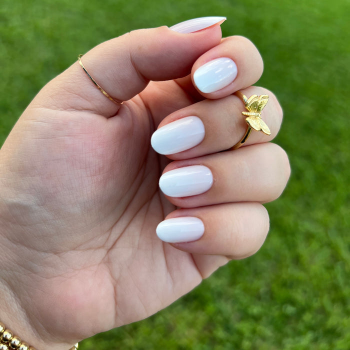 Hand with oval-shaped nails painted glossy pale white held against blurred green grass background