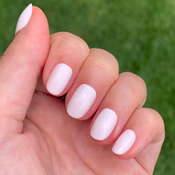Hand with soft sheer pink nails in an extra short round shape from CCT | Round | Extra Short press-on set
