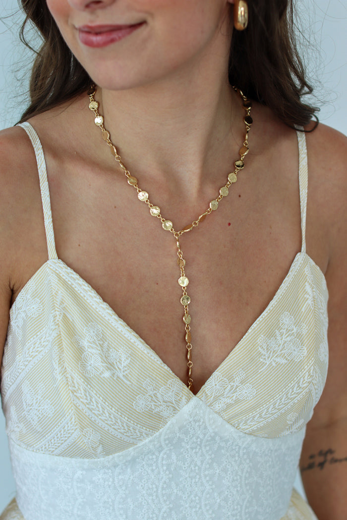 Woman wearing a gold necklace with a white dress against a light background