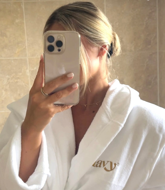 Person wearing a white robe with a logo, holding a phone in a bathroom.