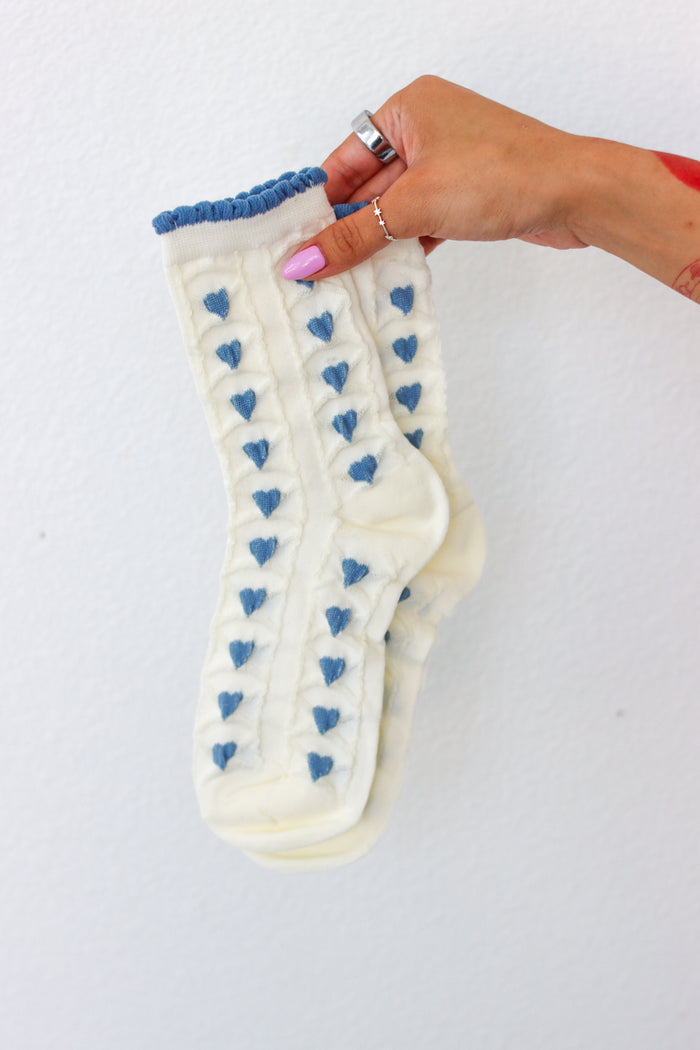 White socks with blue heart patterns held by a hand on a white background