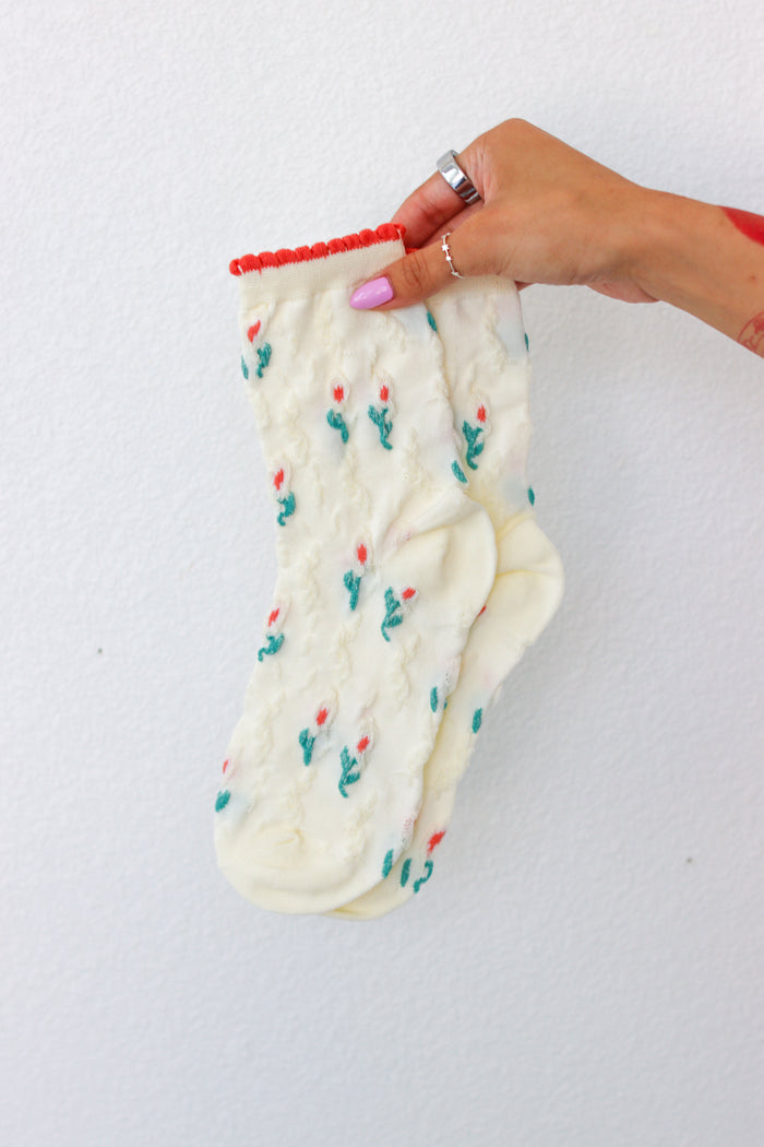 White sock with flower pattern held by a hand on a white background