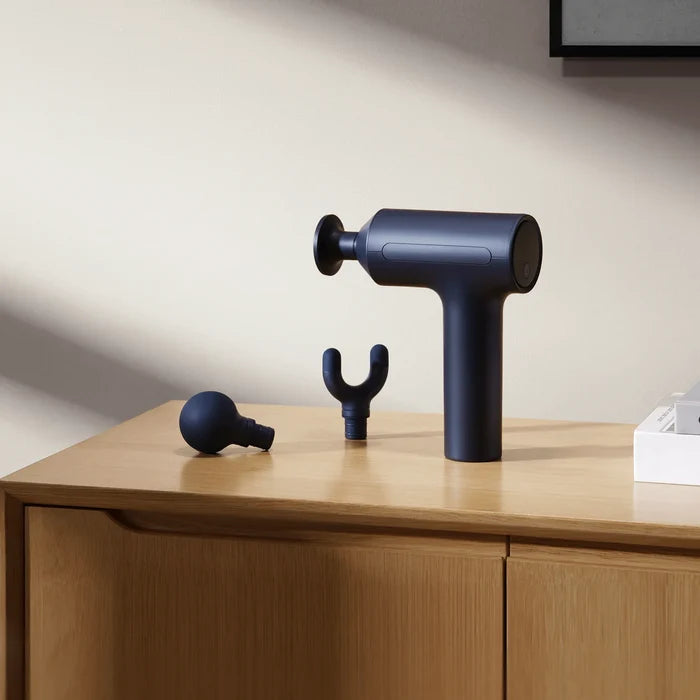 Xiaomi Massage Gun 2 op een houten kast met de ronde en de U-vormige opzetkop